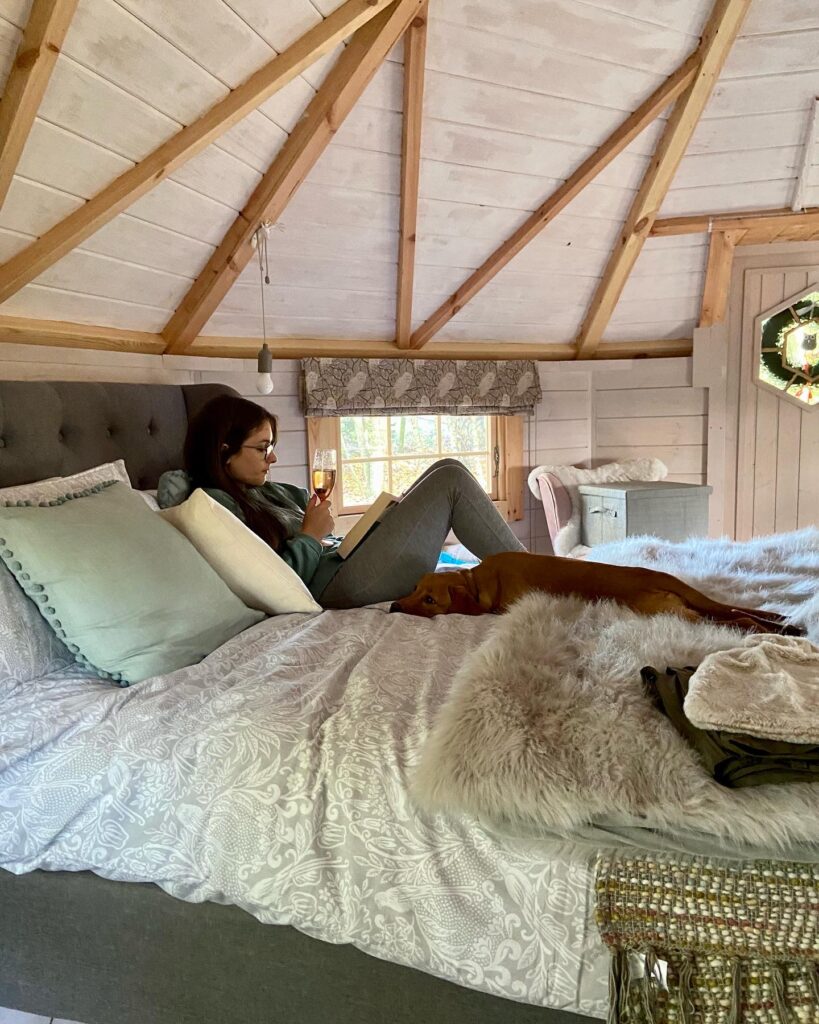 a woman reading on the bed with a dog lying next to her